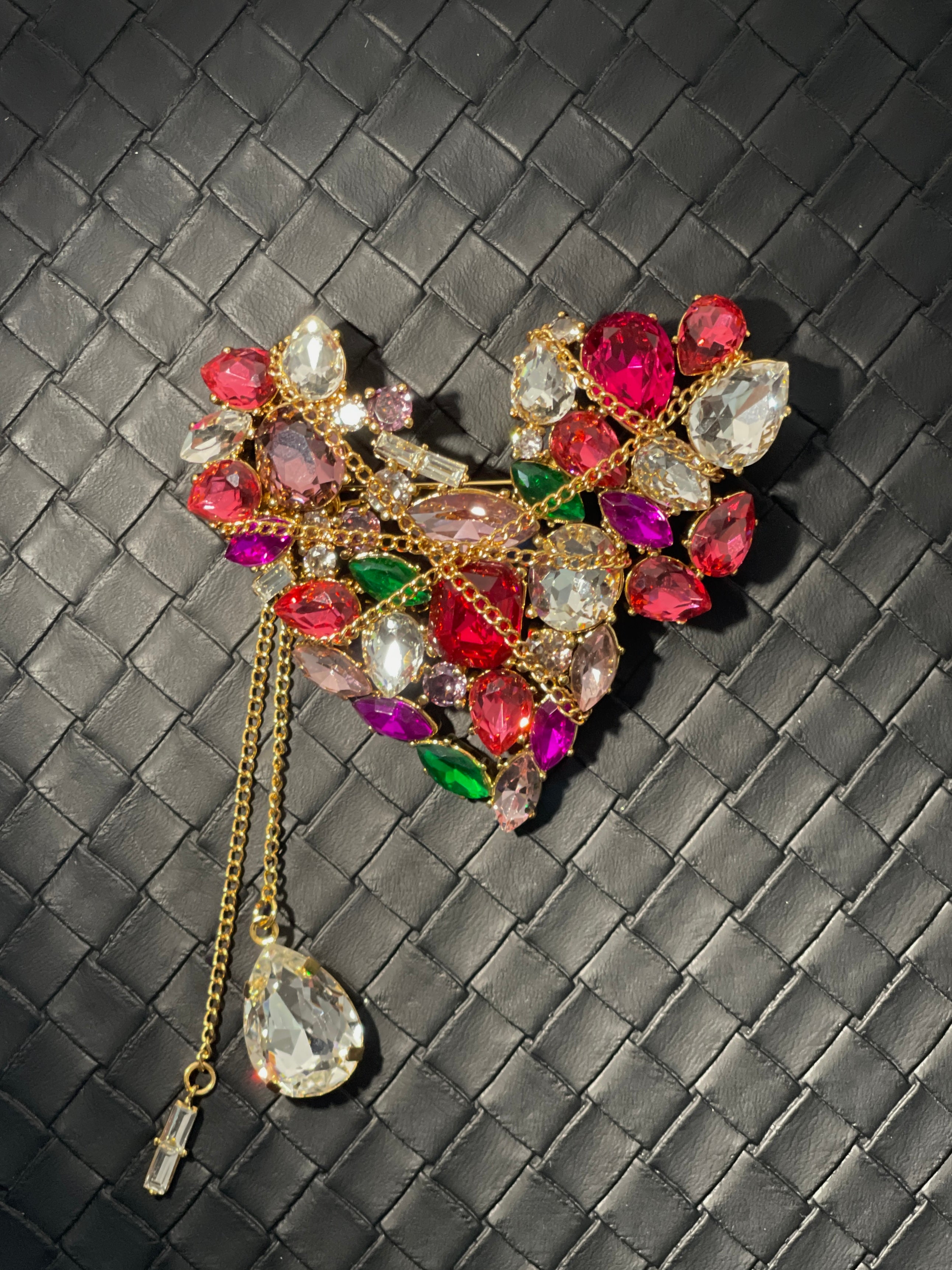 Close-up of vintage-inspired heart brooch with pink, red, green and clear crystal stones, gold-tone chain detail and crystal drop tassel.
