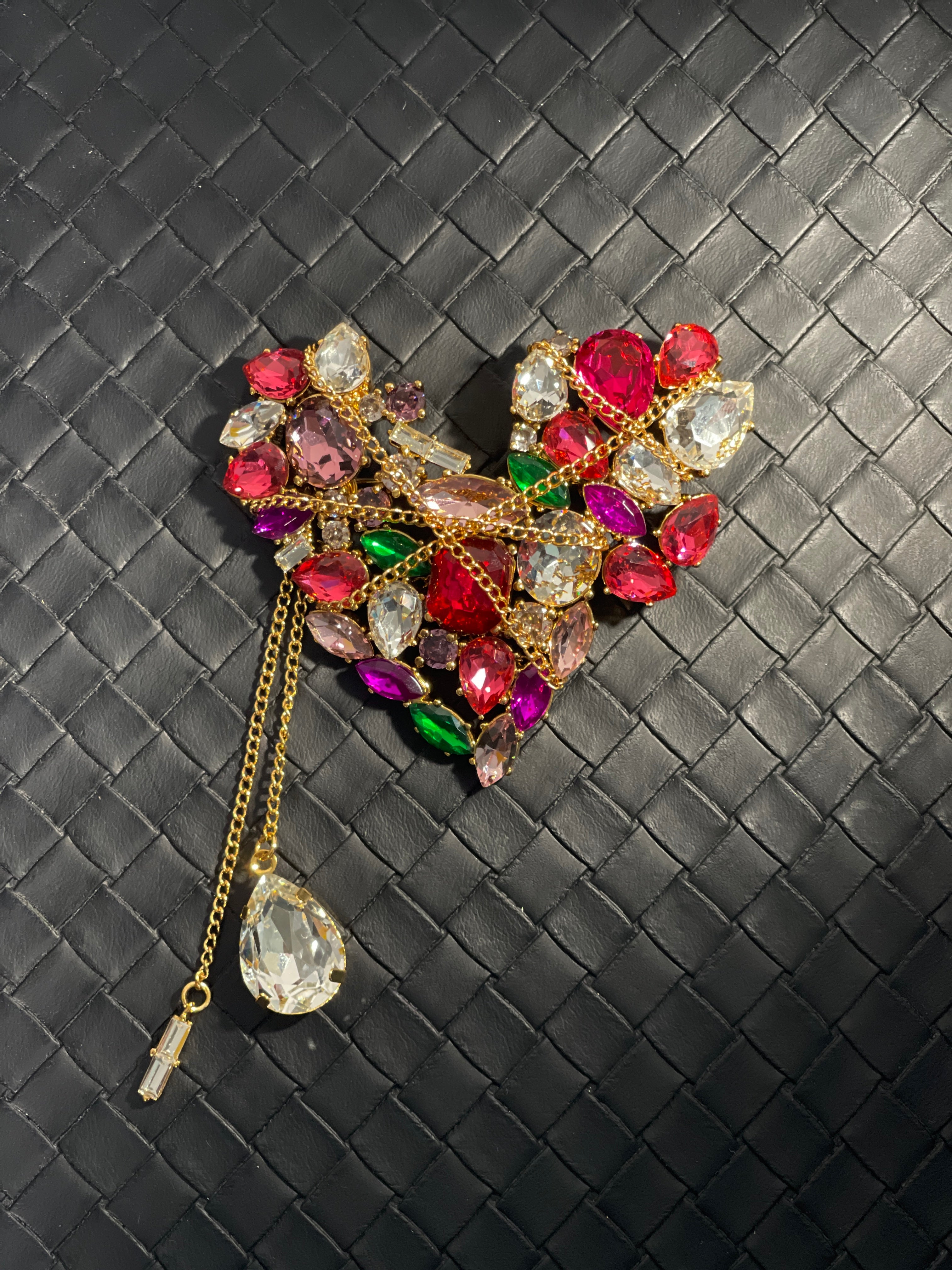 Statement heart brooch in gold-tone metal, decorated with colourful faceted crystals and hanging chain tassels.