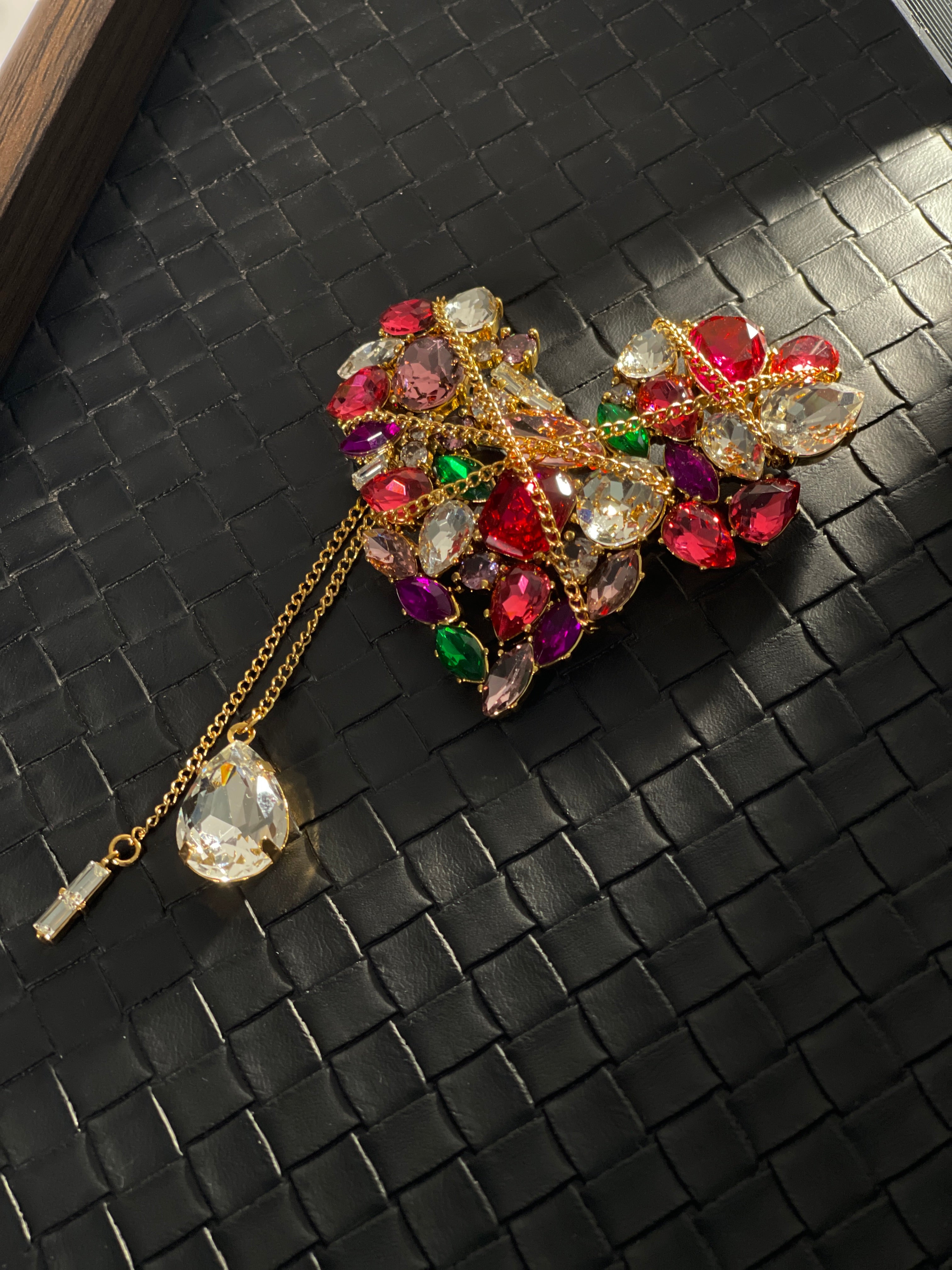 Side view of ornate heart-shaped crystal brooch with gold-tone chains, colourful stones and clear crystal drop pendant.