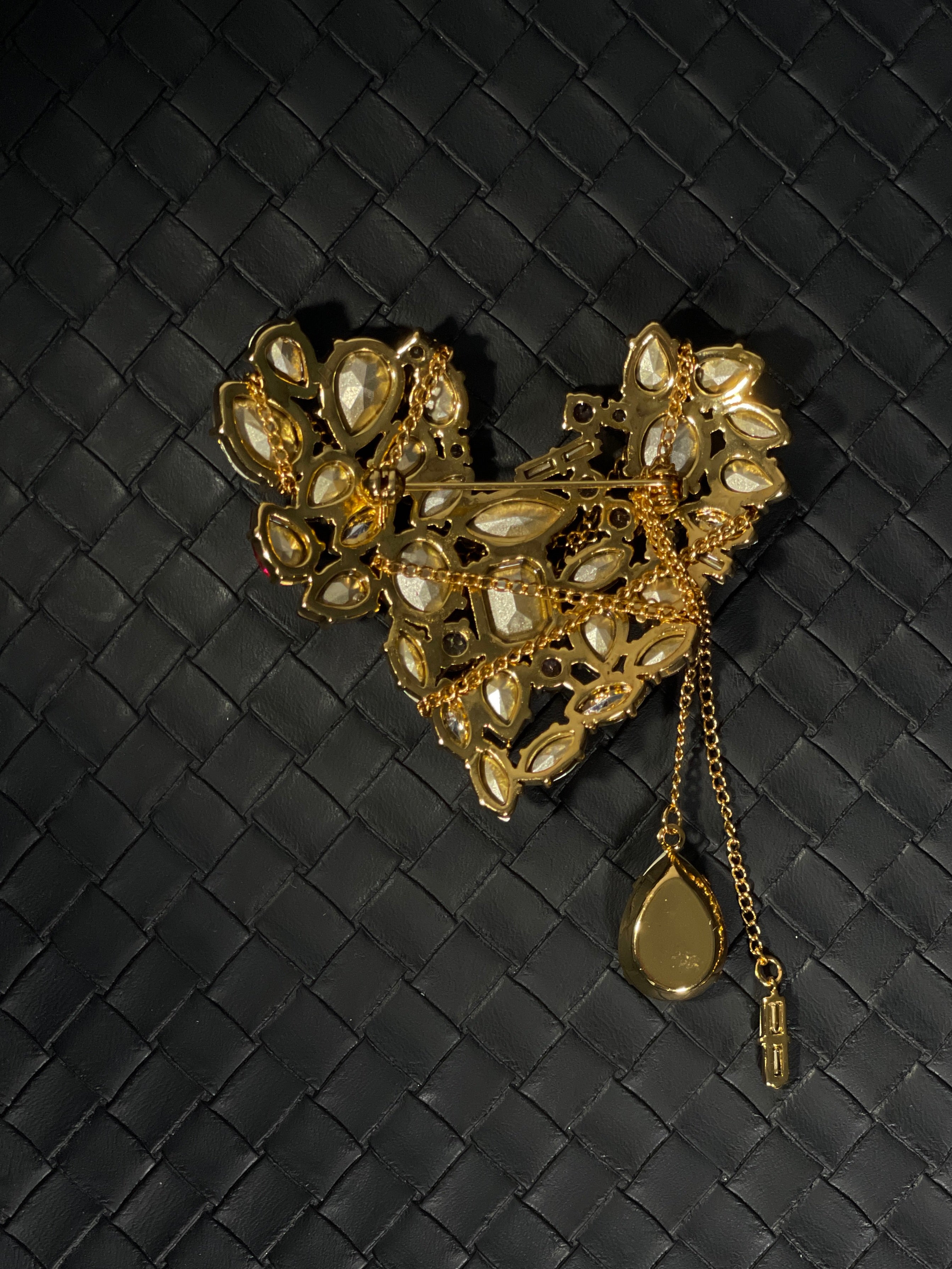 Back view of heart-shaped gold-tone brooch showing pin fastening, openwork setting, crystal backs and hanging chain details.